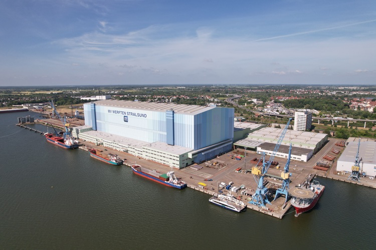 Luftaufnahme eines Hafengeländes mit angedockten Schiffen und angrenzenden Industriegebäuden, Fokus auf technische Infrastruktur am Wasser.