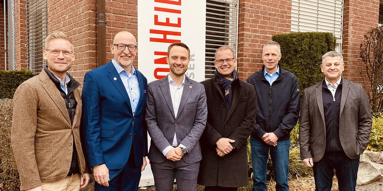 Sechs Männer in Businesskleidung vor Ziegelgebäude und haustec.de-Event-Schild bei Branchentreffen der Gebäudetechnik.