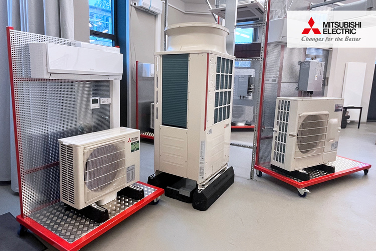 Drei Mitsubishi Electric Klimageräte werden auf roten Transportwagen bei einer Fachmesse für Gebäudetechnik vorgestellt.