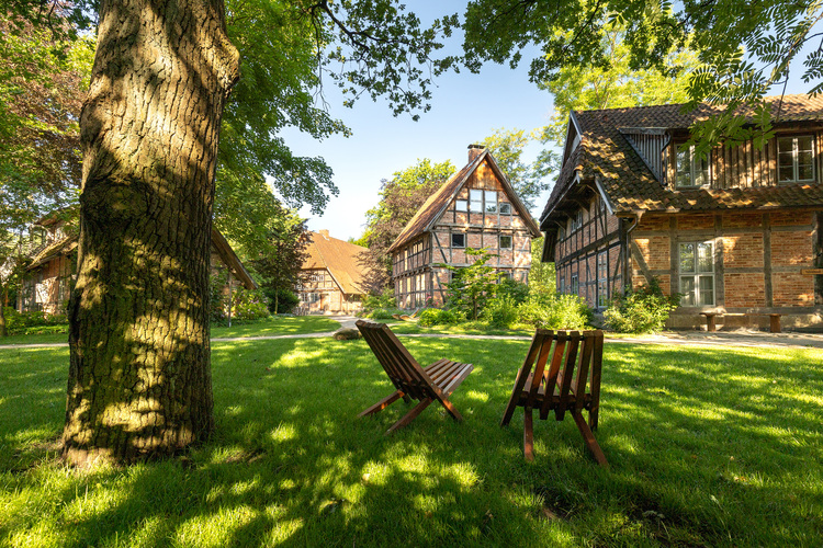 Außenbereich eines energieeffizienten Fachwerkhauses mit gepflegtem Grün, Sitzgelegenheiten und Fokus auf nachhaltige Gebäudetechnik im ländlichen Raum.