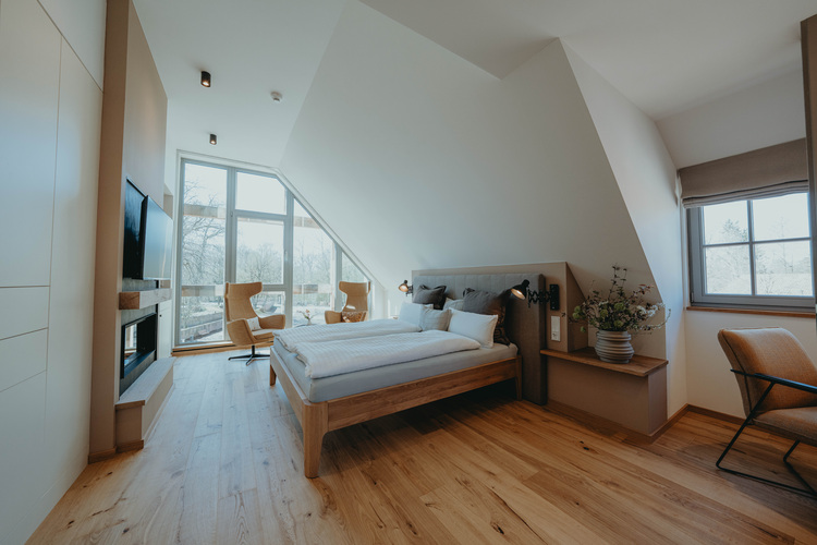 Modernes Schlafzimmer mit schräger Decke, großflächigen Fenstern und Parkettboden, zeigt energieeffiziente Gebäudetechnik-Integration.