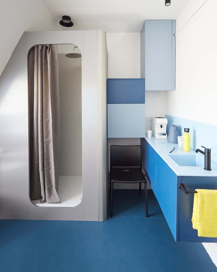 Modernes Bad mit bodengleicher Dusche, blauen Waschtischunterschränken, barrierefreiem Zugang und kontrastreichen Elementen für hohe Funktionalität.