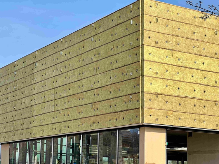 Rohbau eines Gebäudes mit gelben Wärmedämmverbundsystem-Paneelen an der Fassade, Fokus auf energieeffizienter Gebäudehülle im TGA-Kontext.