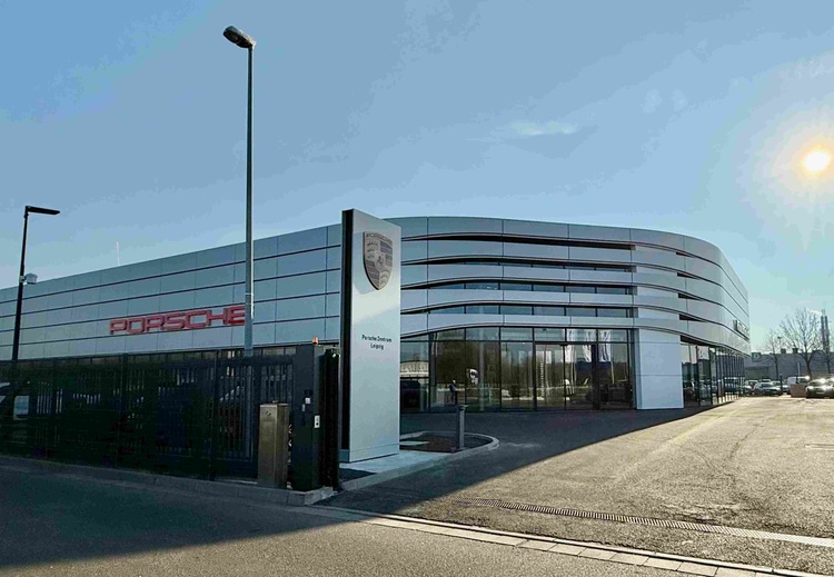 Porsche Autohaus mit moderner, gebogener Glasfassade und großem Logo; Beispiel für zeitgemäße Gebäudehülle im Bereich Gewerbeimmobilien.