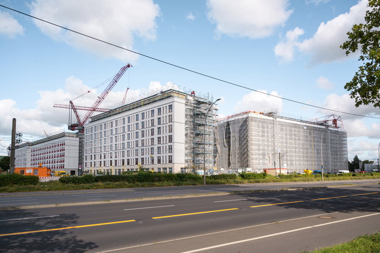 Mehrgeschossige Büro- und Wohngebäude im Rohbau mit Kränen und Gerüsten an einer Straße - Fokus auf moderne Gebäudetechnik in der Bauphase.