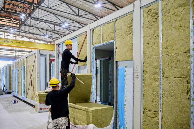 Zwei Fachkräfte montieren Dämmplatten im Innenraum eines modularen Gebäudes - Detailaufnahme zur energetischen Gebäudehülle im Neubau.