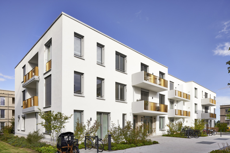 Modernes Mehrfamilienhaus mit weißen Fassaden, großen Fenstern und Balkonen; Fokus auf energieeffiziente Gebäudetechnik und moderne Architektur.