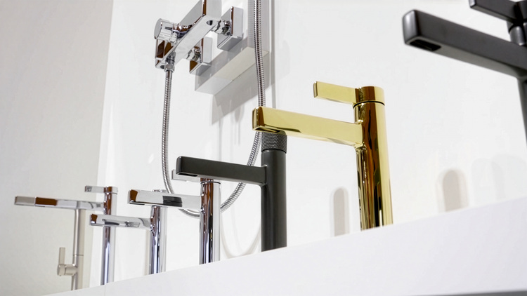 Drei moderne Badarmaturen in Chrom, Schwarz und Gold auf weißem Regal - Designvielfalt für zeitgemäße Bäder in der Gebäudetechnik.