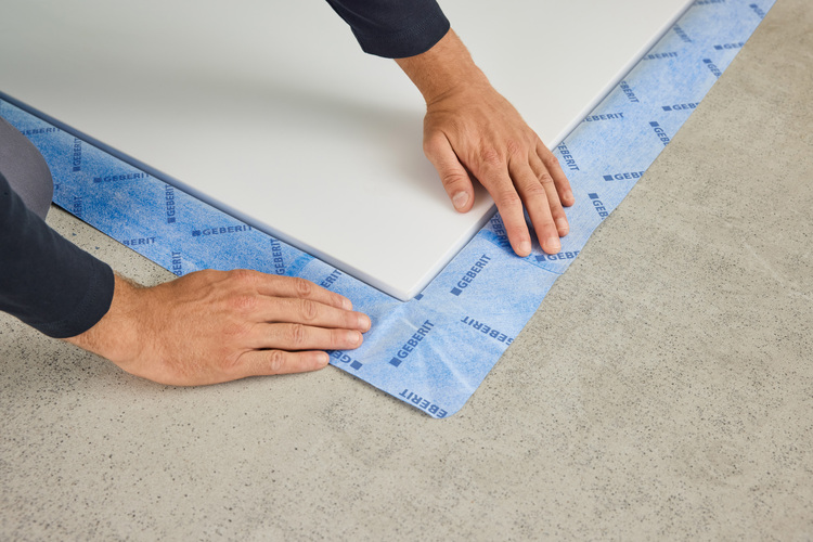 Montage einer weißen Vorwandinstallationsplatte auf einer blauen Geberit-Abdichtbahn, ausgerichtet auf Betonestrich im Sanitärbereich.