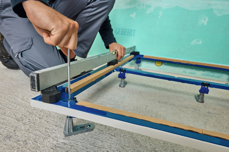 Fachhandwerker montiert mit Schraubendreher eine Metallrahmenkonstruktion auf Betonboden - Montagearbeiten im Gebäudetechnik-Bereich.