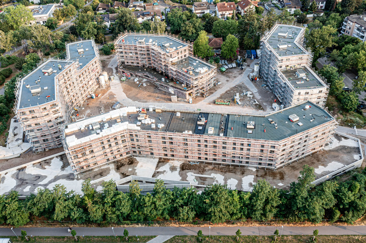 Luftaufnahme eines modernen Mehrfamilienhaus-Neubaus, Fokus auf Baufortschritt, Gebäudetechnikinstallation und energieeffiziente Planung.