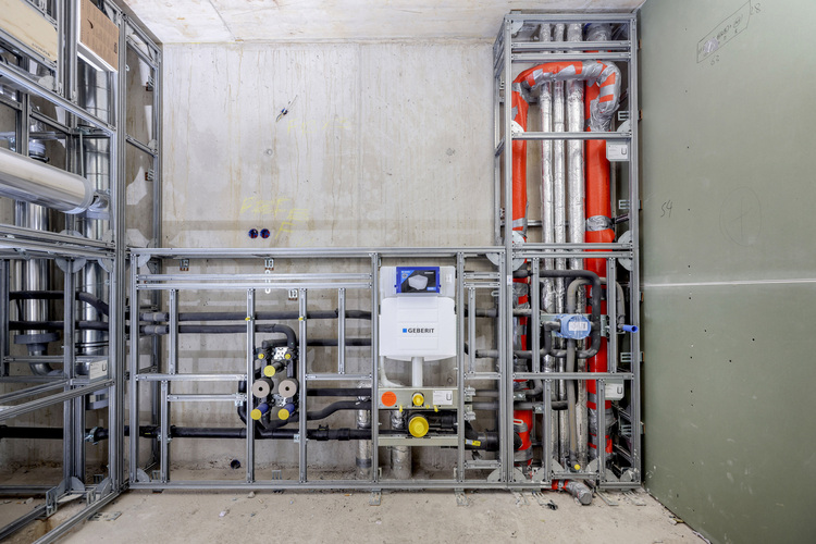 Freiliegende, gedämmte Rohrleitungen und Geberit-Vorwandelement in Rohbauwand; Fokus auf Sanitärinstallation im Neubau.