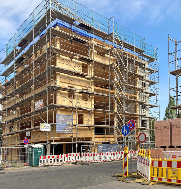 Mehrstöckiges Gebäude im Rohbau mit Gerüst und Absturzsicherungen; Fokus auf Gebäudetechnik-relevante Bauphase, sonniger Tag.
