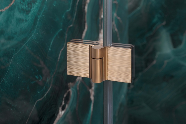 Detailansicht eines gebürsteten Gold-Scharniers, montiert an einer Glaswand, vor grünem Marmor - Beispiel für hochwertige Beschlagtechnik im Innenausbau.