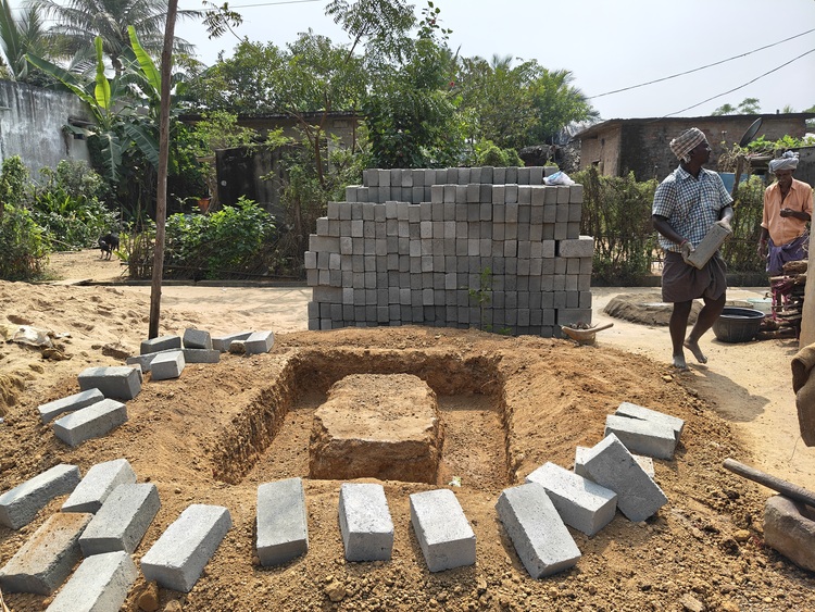 Baustelle in der Gebäudetechnik mit gestapelten Betonsteinen, Fachkräften bei Montagearbeiten und rechteckiger Baugrube für SHK-Installation.