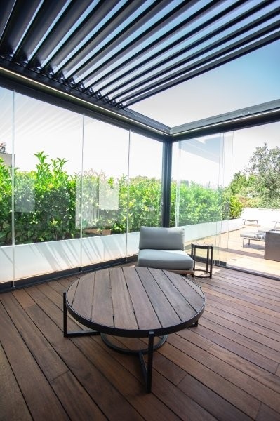 Moderne Terrasse mit Holzfußboden, runder Besprechungstisch, Polsterstuhl und Glasfassade als Beispiel zeitgemäßer Gebäudetechnik und Hülle.