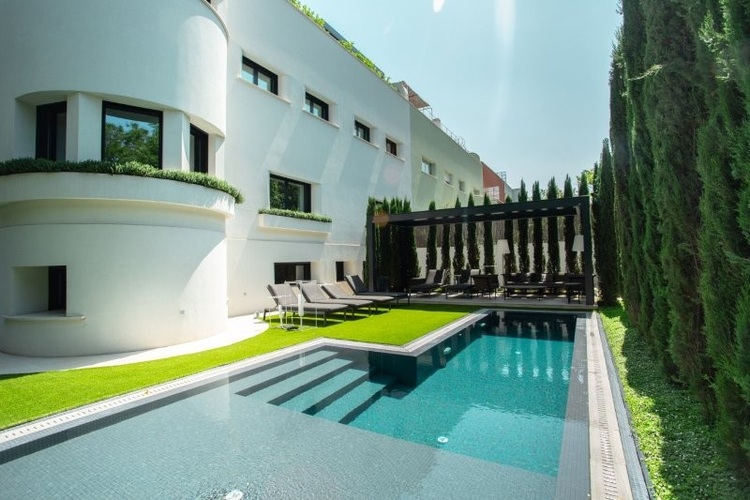 Modernes Wohngebäude mit geschwungenen weißen Fassaden, rechteckigem Pool und Freifläche; Beispiel für energieeffiziente Gebäudetechnik im Außeneinsatz.