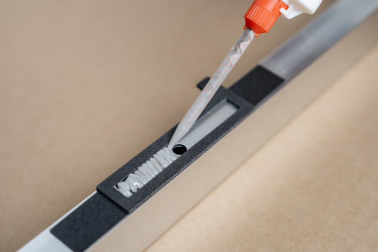 Ausbringen von Montagekleber mit einer Kartuschenpistole in einem schmalen Metallkanal mit Schaumstoffeinlage zur luftdichten Leitungsinstallation.