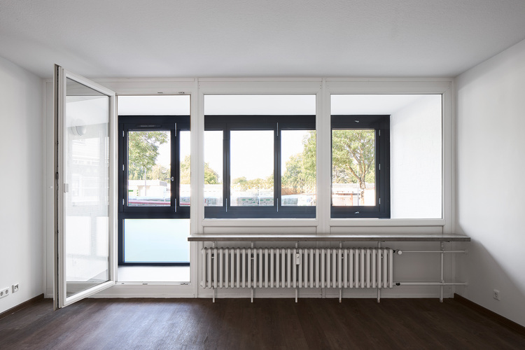 Heller Raum mit großen Fenstern, weißen Wänden, dunklem Holzboden und Heizkörper - Beispiel moderner Heiztechnik in energieeffizientem Gebäude.