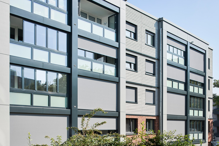Moderne Wohnanlage mit großen Fenstern und Balkonen, energieeffiziente Fassadengestaltung, relevantes Beispiel für innovative Gebäudetechnik.