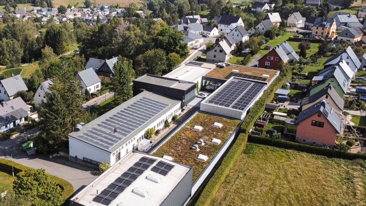 Drohnenaufnahme: Wohngebäude mit Photovoltaikanlagen auf den Dächern, umgeben von Grünflächen - Beispiel für energieeffiziente Quartiersentwicklung.