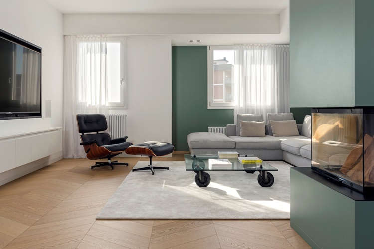 Modernes Wohnzimmer mit grauem Ecksofa, Kamin und Glas-Couchtisch, zeigt beispielhafte Einrichtungslösungen für energieeffiziente Gebäudetechnik.