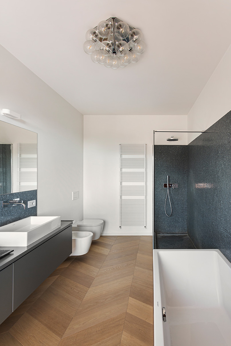 Barrierefreies, modernes Bad mit schwarzer Dusche, weißer Wanne, Bidet, WC, großem Spiegel und hölzernem Fischgrätboden für effiziente Gebäudetechnik.
