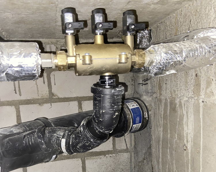 Detailansicht eines Rohrleitungsanschlusses mit Absperrventilen in einem Technikraum mit Betonwand, typische Installation in der Gebäudetechnik.