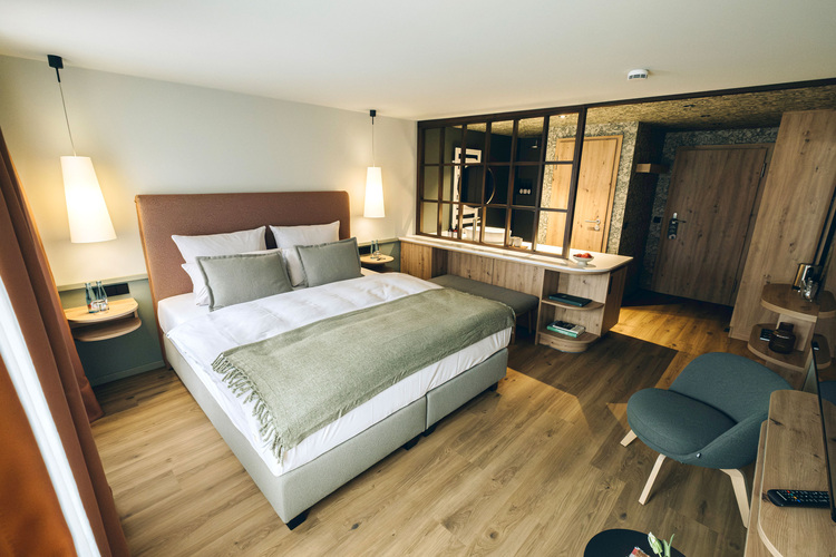 Barrierefreies Hotelzimmer mit großer barrierearmer Liegefläche, Holzmöbeln, blendfreier Beleuchtung und reduziertem Design für Gebäudetechnik.
