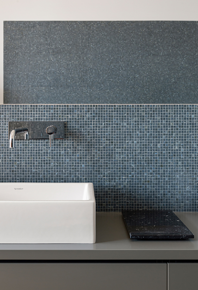 Waschtisch mit wandmontierter Armatur, blauer Mosaikfliesen-Rückwand und schwarzem Ablage-Tablett, geeignet für moderne Sanitärkonzepte.