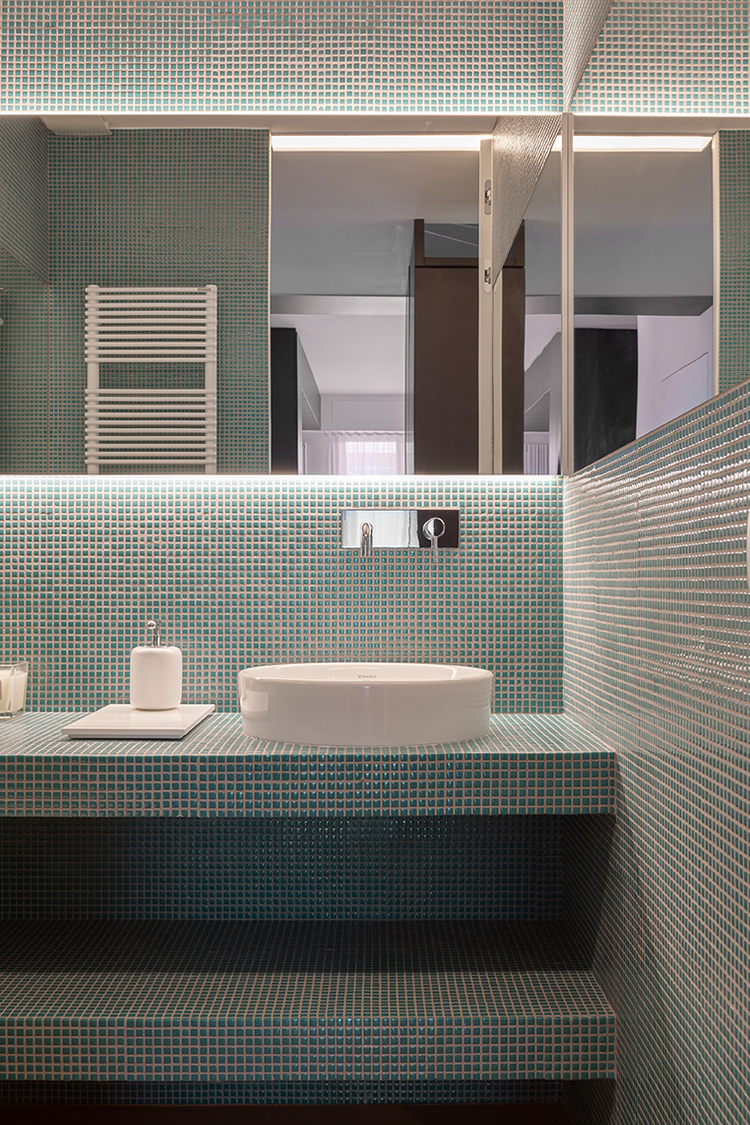 Modernes Bad mit grünen Mosaikfliesen, rundem Waschbecken, Spiegel und wandmontiertem Handtuchwärmer - Beispiel für moderne Sanitärinstallation.