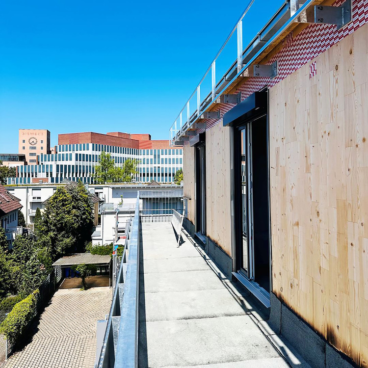 Flachdach mit Holzpaneelen im Aufbau, Blick auf Gebäude und Bäume; Beispiel für Dachsanierung und energieeffiziente Gebäudehülle.