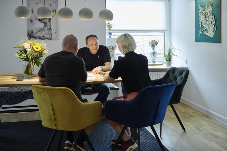 Drei Fachleute diskutieren an einem Konferenztisch in einem modernen, gut beleuchteten Raum über Gebäudetechnik-Lösungen.