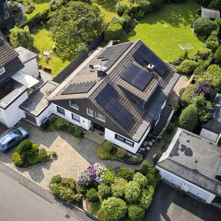 Luftaufnahme eines Einfamilienhauses mit PV-Anlage auf dem Dach, energieeffizienter Gebäudehülle und begrünter Außenanlage als Praxisbeispiel für Gebäudetechnik.