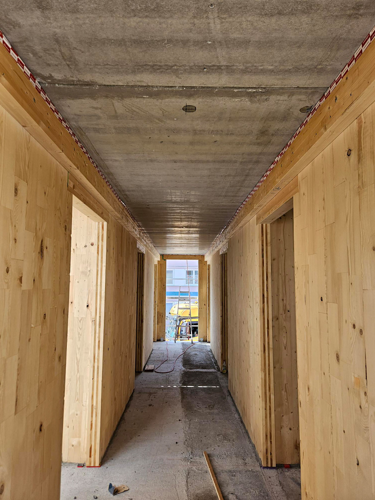 Rohbau-Flur mit Holzständerwänden und Betondecke; Blick in offenen Bereich mit Bauwerkzeugen, typisch für Gebäudetechnik-Baustellenphase.