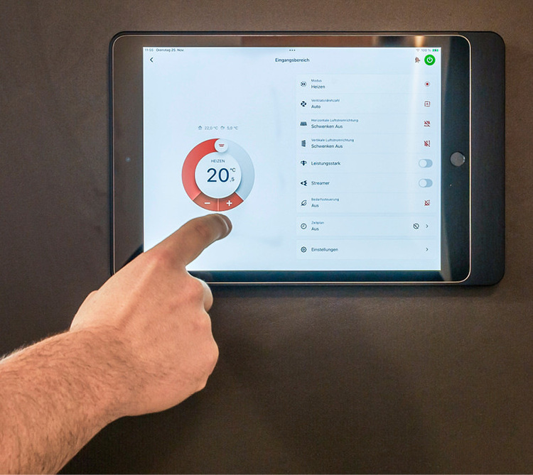 Hand justiert digitale Heizungssteuerung auf Wand-Tablet im modernen Gebäude, stellt Raumtemperatur auf 20 °C für energieeffizientes Klima ein.