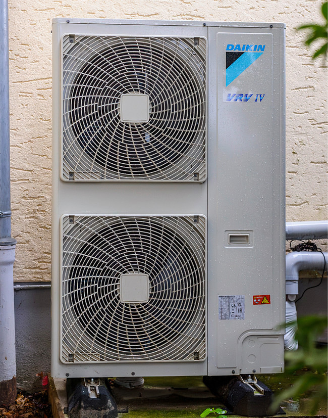 Daikin VRV IV Außengerät mit zwei großen Ventilatoren, installiert vor beiger Wand - Beispiel moderner Klimatechnik für energieeffiziente Gebäude.