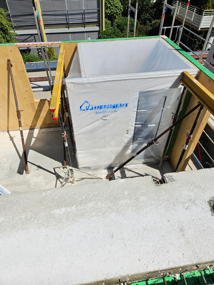 Baustelle mit eingerüstetem, abgedecktem Aufzugsschacht; sichtbare Holzträger und Gerüst, typische Situation im Rohbau eines Technikgebäudes.
