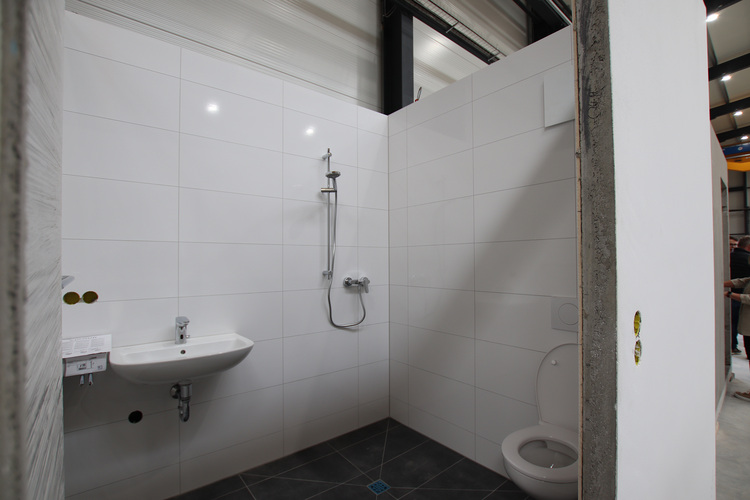 Barrierefreies, gefliestes Bad mit wandmontiertem Waschtisch, bodengleicher Dusche und WC - geeignet für moderne Gebäudetechnik-Konzepte.