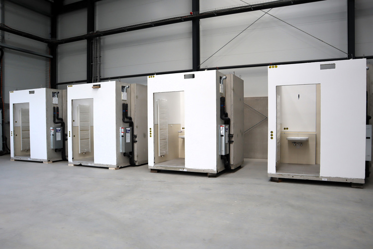 Vier vorgefertigte Sanitärmodule mit Waschbecken zur flexiblen Installation stehen in einer leeren Industriehalle für Gebäudetechnik-Musterpräsentation.
