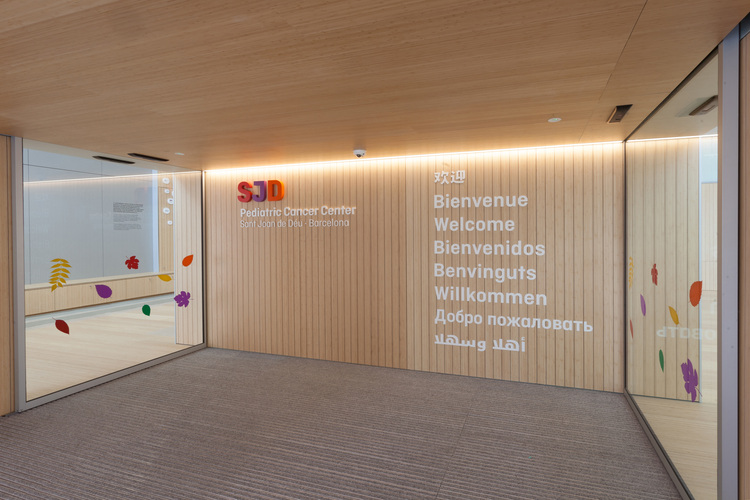 Barrierefreier, modern gestalteter Flur mit großflächiger Holzverkleidung und mehrsprachiger Willkommensprojektion, repräsentativ für Gebäudeintegration.