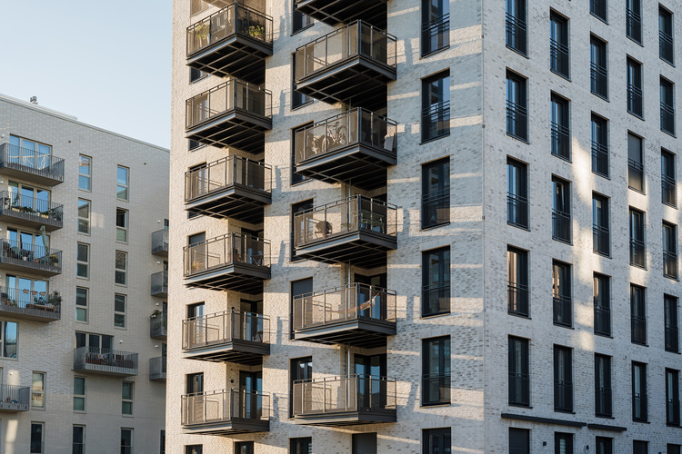 Mehrgeschossiges Wohngebäude mit hell verklinkerter Fassade und mehreren Balkonen, Beispiel für energieeffiziente Gebäudehülle und moderne TGA.