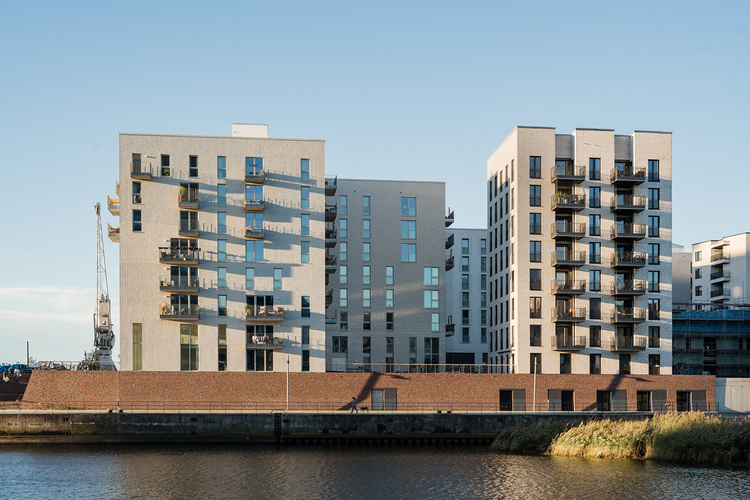 Zwei moderne Mehrfamilienhäuser mit Balkonen an einer Uferpromenade, geeignet für energieeffiziente Gebäudetechnik und nachhaltige Wohnkonzepte.