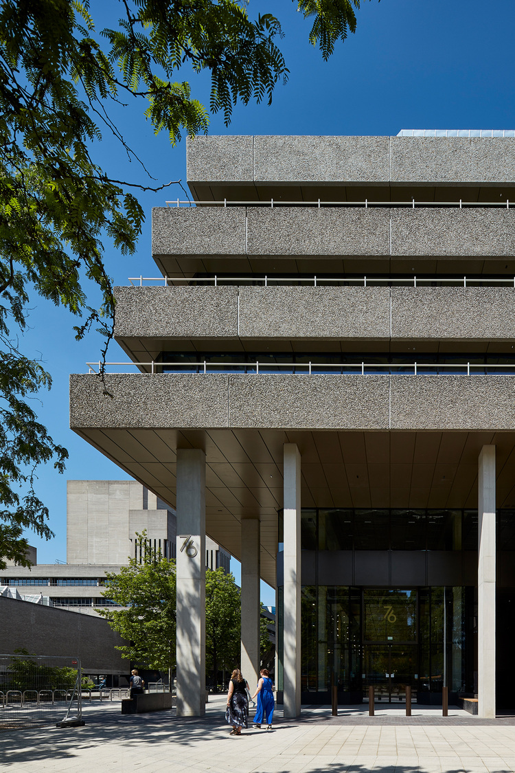 Moderne brutalistische Gewerbeimmobilie mit weit auskragenden Betondecken, breiten Stützen und Glasfassade am Eingang, relevante Gebäudetechnik.