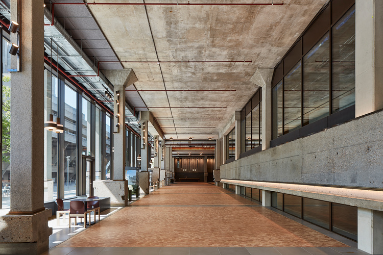 Moderner Gebäudeflur mit Beton-Decke, großen Glasfenstern und minimalistischen Sitzbänken, geeignet für energieeffiziente Gebäudetechnik.
