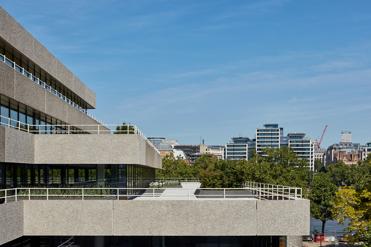 Modernes Geschäftsgebäude mit strukturierter Betonfassade, Stadtbäumen und Skyline bei Tageslicht - Fokus auf innovative Gebäudetechnik.