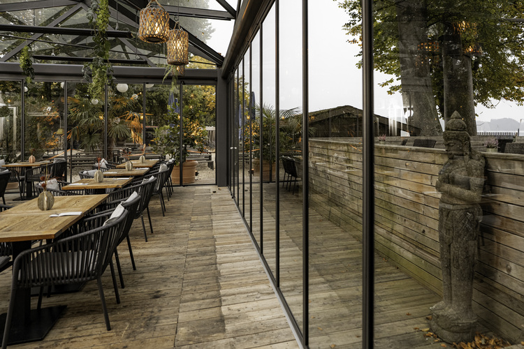 Modern gestalteter Außenbereich eines Gastronomiebetriebs mit Holzboden, Glasfassade und Begrünung als Beispiel für energieeffiziente Gebäudetechnik.