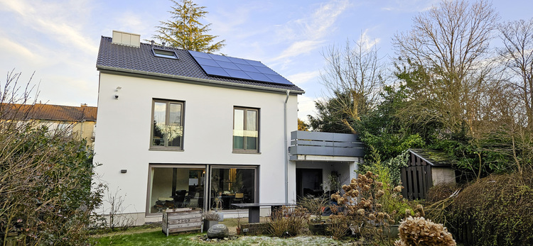 Modernes Einfamilienhaus mit Photovoltaikanlage auf dem Dach, umgeben von Begrünung - Beispiel für energieeffiziente Gebäudetechnik und Nachhaltigkeit.
