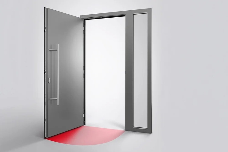 Eine geöffnete graue Tür in einem modernen Gebäude; rotes Licht als Sicherheits- oder Fluchtwegbeleuchtung strahlt halbkreisförmig auf den weißen Boden.