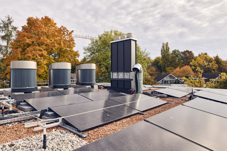 Gebäudedach mit Photovoltaikanlage und Klimaanlagen, im Hintergrund herbstliche Bäume – Schwerpunkt auf Energieeffizienz in der modernen Gebäudetechnik.
